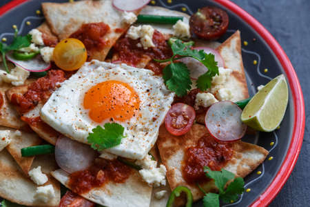 Mexican breakfast: chilaquiles with egg, avocado and vegetables close-up on a plateの写真素材