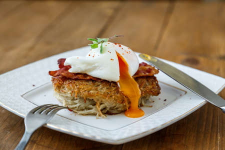 Potato rosti, poached egg with runy yolk and bacon on top.の写真素材