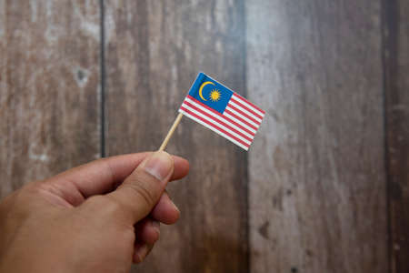 Holding Malaysia mini flag with blur wooden wallpaperの写真素材