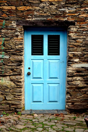 Rustic hand-hewn wood door set into a stone wall built from schist in Piodão, made of shale rocks...
