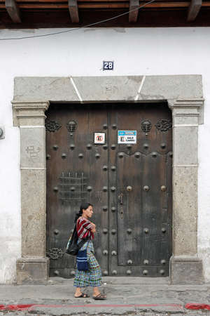 Antigua, Guatemala 03-01-2008 A local woman in traditional dress walks past an antique doorway on a street in Antigua.のeditorial素材