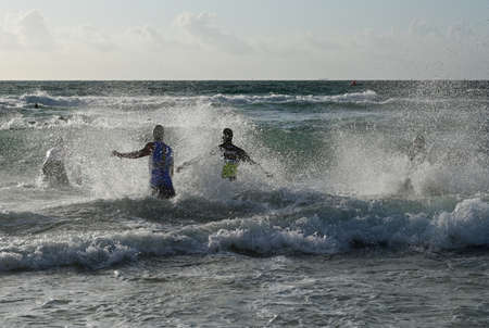 Miami Beach, Florida April 14, 2019 Male triathletes run into heavy surf at the start of the 2019 South Beach Triathlon.のeditorial素材
