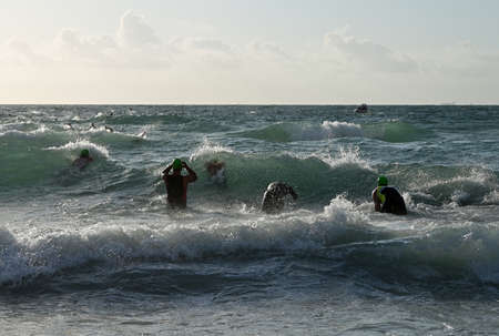 Miami Beach, Florida April 14, 2019 Male triathletes run into heavy surf at the start of the 2019 South Beach Triathlon.のeditorial素材