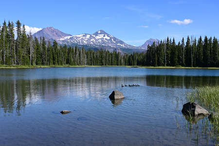 Middle and North Sisters volcanoes reflected in the still water of Scott Lake on a clear and sunny...