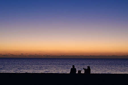 Sitting couple silhouetted against pastel colors of twilight waiting for sunrise on Crandon Park...