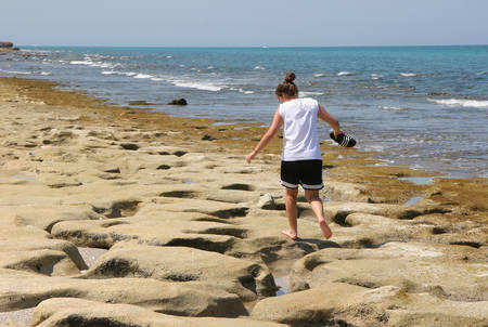 Young woman explores tide pools and rock formations of Coral Cove Park in Tequesta, Florida at extreme low tide on clear cloudless afternoon.の写真素材