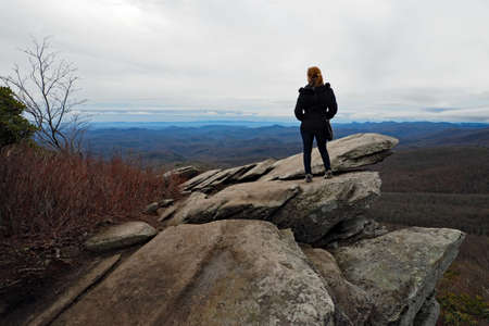 Blowing Rock, North Carolina - January 2, 2015: Woman looks over layered mountains standing on rock outcropping on cold winter morning.のeditorial素材