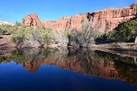 Red rock formations reflected in tranquil pond in Sedona, Arizona backcountry on clear cloudless winter afternoon.の写真素材