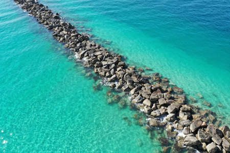 Aerial view of rock jetty of Government Cut surrounded by clear shallow water of Miami Beach,...