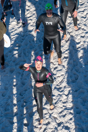 Panama City Beach, Florida - November 4, 2023 - Young woman athlete runs onto beach after completing swim portion of 2023 Ironman competition.のeditorial素材