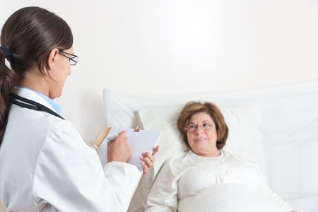 Standing Doctor writes prescription to Senior Patient lying in bedの写真素材