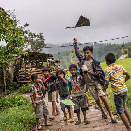 Mamasa, South Sulawesi, Indonesia - August 17, 2014: Local group of 6 children and 1 teen enjoying to play with kite in a cloudy rainy day.のeditorial素材
