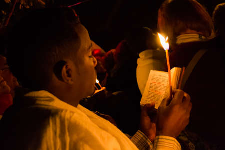 Gonder, Ethiopia - January 20, 2012: priest holding a candle in the night and reading a book written in the old language of the church, called Geez, during the Timkat holiday, the important Ethiopian Orthodox celebration of Epiphany.のeditorial素材