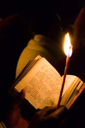 Gonder, Ethiopia - January 20, 2012: priest holding a candle in the night and reading a book written in the old language of the church, called Geez, during the Timkat holiday, the important Ethiopian Orthodox celebration of Epiphany.のeditorial素材