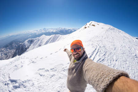 Adult alpin skier with beard, sunglasses and hat, taking selfie on snowy slope in the beautiful italian Alps with clear blue sky. Concept of wanderlust and adventures on the mountain. Wide angle fisheye lens.の写真素材