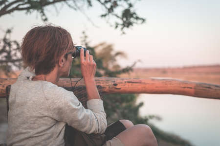 Tourist watching wildlife by binocular on Chobe River, Namibia Botswana border, Africa. Chobe National Park, famous wildlilfe reserve and upscale travel destination. Toned image.の写真素材