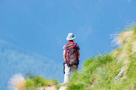 Backpacker walking on hiking trail in the mountain. Summer adventures summer vacation on the Alps....