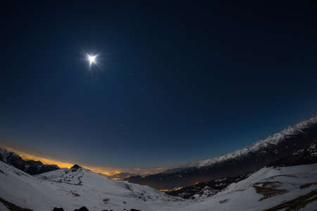 Turin city lights, night view from snow covered Alps by moonlight. Moon and Orion constellation, clear sky, fisheye lens. Italy.の写真素材