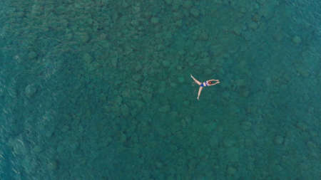 AERIAL: woman floating on blue water surface, swimming in transparent mediterranean sea, top down...