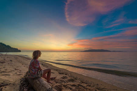 Woman relaxing on sand beach romantic sky at sunset, rear view, golden cloudscape, real people. Indonesia, Kei islands, Moluccas Malukuの写真素材