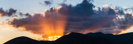 Sunset view point on rocky mountains silhouette. Campo Imperatore, Gran Sasso, Apennines, Italy. Sun beams and colorful clouds in the sky on dramatic mountain ridge.の写真素材