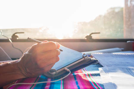 Teacher smart working from a van. Focus on pen. Woman hand close up using tablet digital pen smart phone to teach online. Backlight sun burst.の写真素材