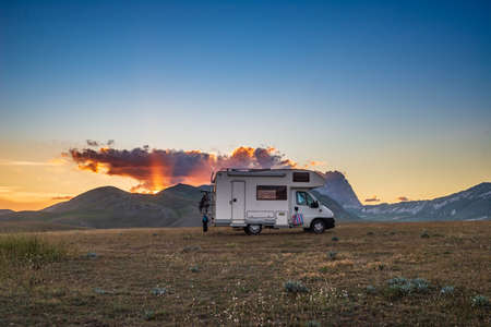 Sunset dramatic sky over camper van in Campo Imperatore highlands, Abruzzo, Italy. Epic clouds above unique highlands and rocky mountains landscape, alternative vanlife vacation concept.の写真素材