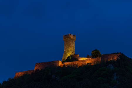Radicofani, a medieval village and fortress in Tuscany, Italy. Unique view at dusk, the stone tower perched on rock cliff illuminated at dusk against blue sky.のeditorial素材
