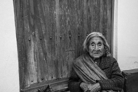 Old woman sitting in front of the door of her house in black and whiteのeditorial素材