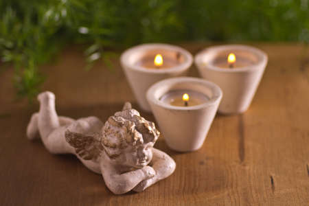 Little sculpture of an angel with three candles on a wooden tableの写真素材