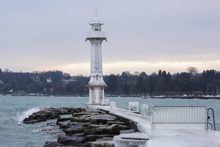 The Paquis pier and lighthouse covered with ice after a winter storm on Lake Geneva, Switzerland.の写真素材