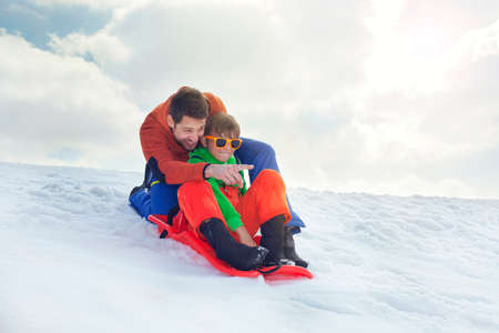 father and son having fun in the snow, slidingの写真素材