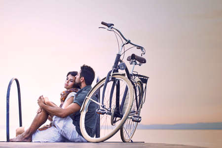 Couple in love resting on a boardwalk with a bike at the lakeの写真素材