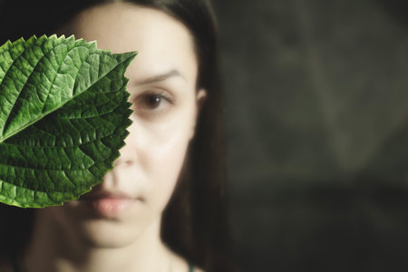 look of a woman hiding her face behind a large leafの写真素材