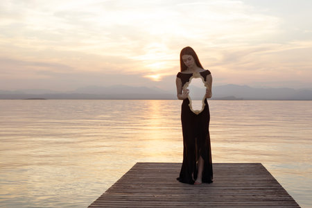 Woman in black dress with mirror in front of the sea: surreal reflections between reality and introspectionの写真素材