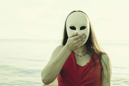elegant woman with mask in front of her face covering her mouth with her handの写真素材