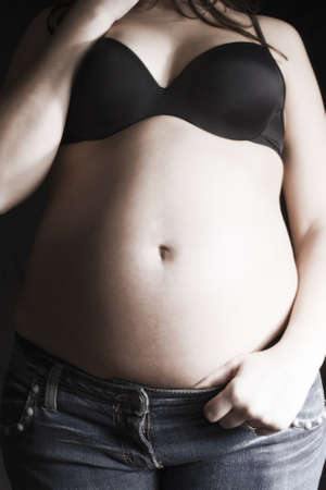 big belly pregnant woman in jeans and black bra on a black backgroundの写真素材