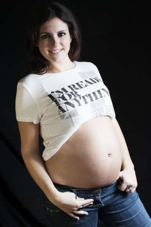 pregnant woman with a jeans and white t-shirt  standing on a black backgroundの写真素材