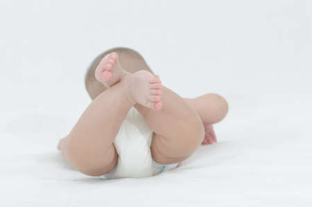 Happy smiling child playing on a white bed, showing her little feetの写真素材