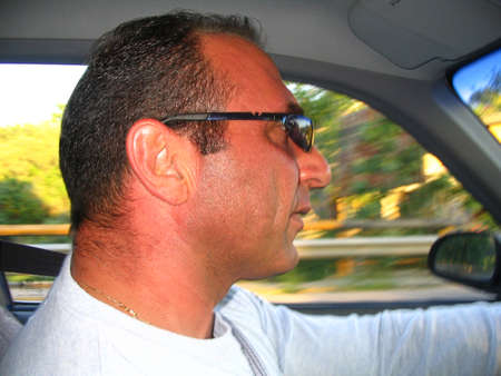 A man while driving. Side headshot. Background blurred