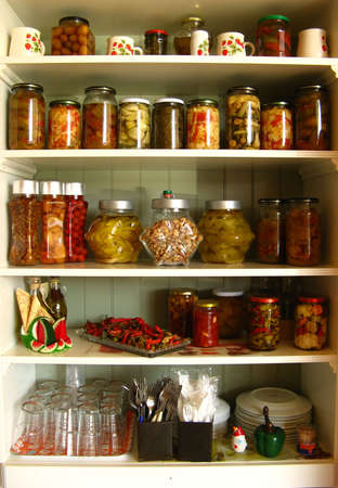 A white kitchen cabinet full of jars, sauces and bottles