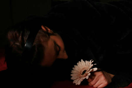 Woman with a pink flower in the dark lit by a flashlightの写真素材