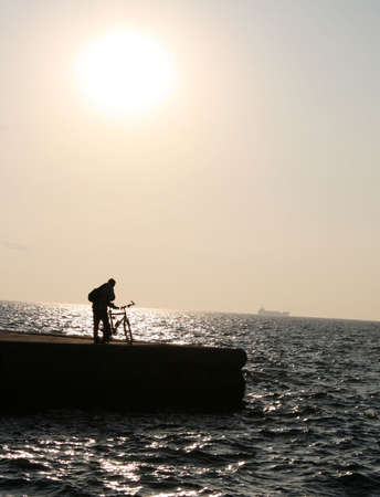 A sillouette of a man with a bicycle at sunsetの写真素材