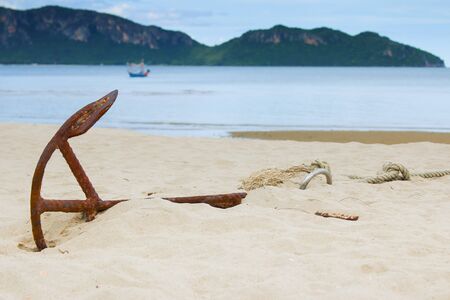 Old anchor on sandy beach with background of sea and mountains.の写真素材