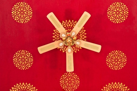 Ceiling fan with five lights on a red ceiling with Thai painted.の写真素材