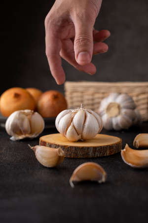 hand took garlic on wooden cutting board with onion and dark backgroundの写真素材
