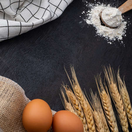 wheat ears, eggs and flour on dark board, top view