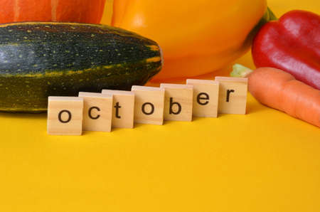 Vegetables on a yellow background. The month of October is written in wooden letters. The calendar. Fall. Harvest.の写真素材