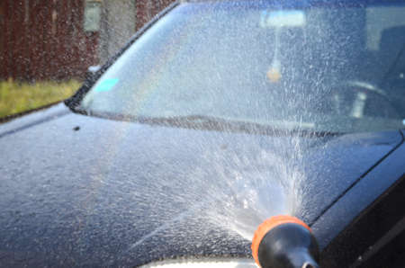Black car washed with shampoo. Water is pouring onto the car. Rainbow on the water.の写真素材
