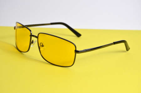 Glasses in metal frames with yellow lenses on a yellow background.
